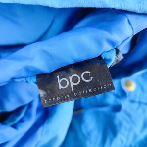 May include: A close-up of a black label with the text "bpc bonprix collection" on a blue jacket.