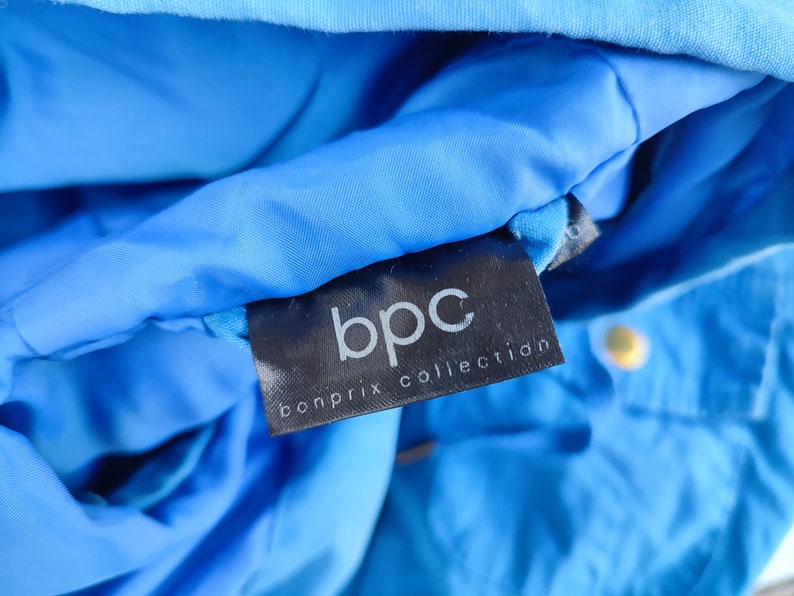 May include: A close-up of a black label with the text "bpc bonprix collection" on a blue jacket.