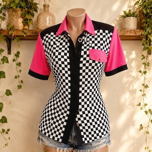 May include: A short-sleeved button-down shirt featuring a black and white chequered pattern on the front and back panels, accented by solid hot pink sleeves, a hot pink collar, and a single chest pocket with a pink flap and a small gold button.