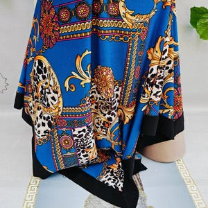 Puede incluir: Un pa&ntilde;uelo azul con un dise&ntilde;o de cadena dorada y estampado de leopardo. El pa&ntilde;uelo tiene un borde negro y presenta detalles dorados ornamentados y acentos florales. La tela est&aacute; drapeada, mostrando el intrincado patr&oacute;n y las variaciones de color.