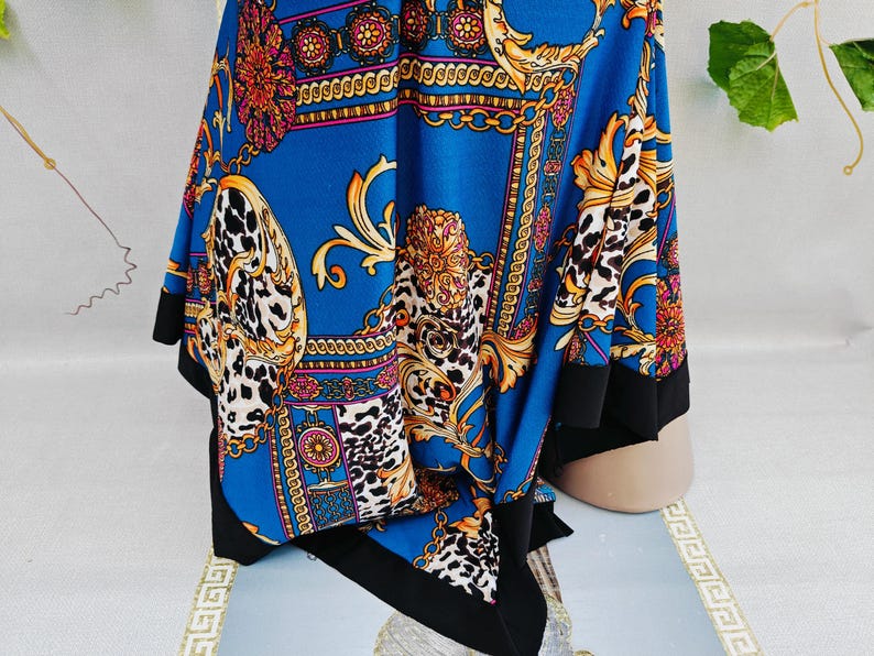 Puede incluir: Un pa&ntilde;uelo azul con un dise&ntilde;o de cadena dorada y estampado de leopardo. El pa&ntilde;uelo tiene un borde negro y presenta detalles dorados ornamentados y acentos florales. La tela est&aacute; drapeada, mostrando el intrincado patr&oacute;n y las variaciones de color.
