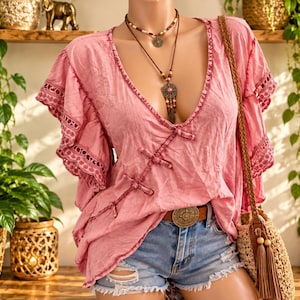 Pode incluir: Uma blusa rosa empoeirado com decote em V profundo, três fechos de tecido e mangas curtas com babados e detalhes em renda. A peça é combinada com um short jeans azul claro e um cinto de couro marrom com uma fivela de metal.
