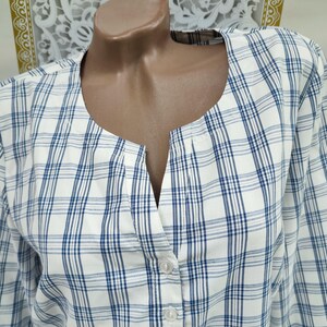 Pu&ograve; includere: Camicia a maniche lunghe a quadri bianchi e blu con scollatura a V e chiusura con bottoni. La camicia &egrave; esposta su un manichino. Il motivo a quadri presenta sottili linee blu su sfondo bianco.