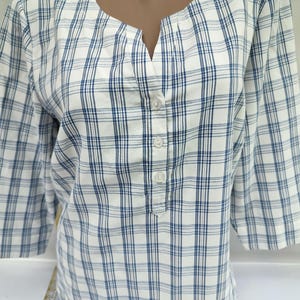 Pu&ograve; includere: Una camicia a quadri bianchi e blu con maniche a tre quarti. La camicia ha uno scollo a V e un'abbottonatura. Il motivo a quadri presenta una griglia di sottili linee blu su sfondo bianco. La camicia &egrave; realizzata in tessuto leggero.
