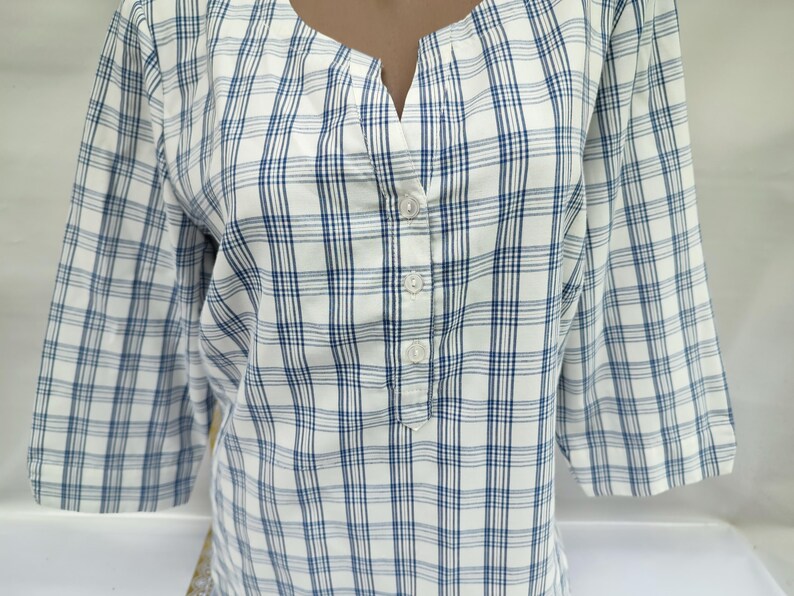 Pu&ograve; includere: Una camicia a quadri bianchi e blu con maniche a tre quarti. La camicia ha uno scollo a V e un'abbottonatura. Il motivo a quadri presenta una griglia di sottili linee blu su sfondo bianco. La camicia &egrave; realizzata in tessuto leggero.