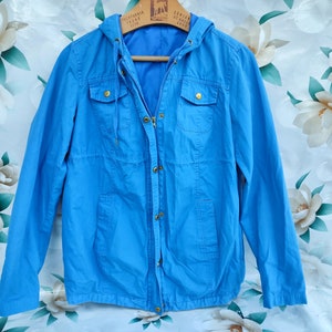 May include: A light blue hooded jacket with a zipper closure and two flap pockets. The jacket has a drawstring hood and a relaxed fit.