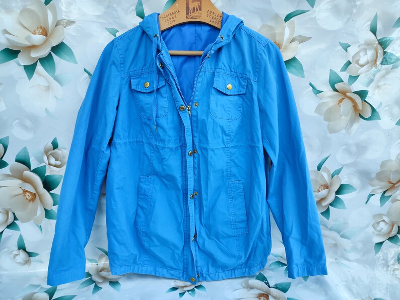 May include: A light blue hooded jacket with a zipper closure and two flap pockets. The jacket has a drawstring hood and a relaxed fit.