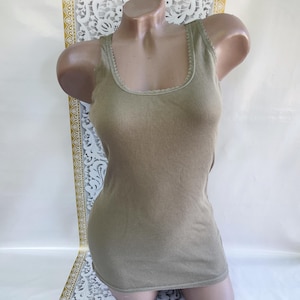May include: Olive green ribbed tank top with a scoop neckline. The tank top is displayed on a mannequin. The fabric has vertical ribbing. The neckline and armholes are trimmed with a delicate, scalloped edge.