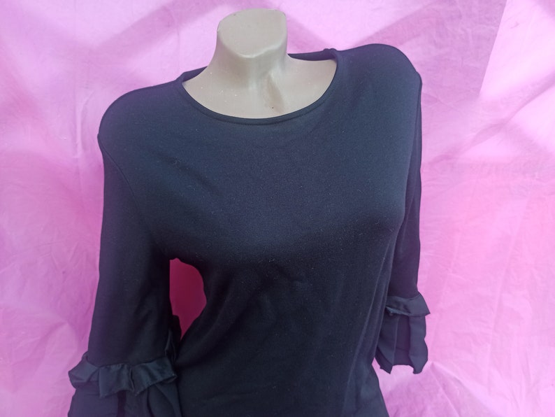 May include: A black long-sleeved shirt with ruffled sleeves. The shirt is made of a soft, stretchy fabric.