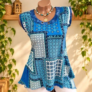 Peut inclure: Un haut bleu sans manches présentant un motif patchwork avec divers designs géométriques et floraux dans des tons bleu marine, turquoise et blanc. L'encolure ronde comprend une bordure effet tie-dye avec deux œillets métalliques sur le devant.