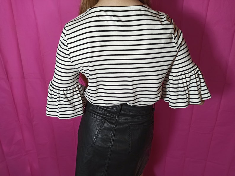 May include: A white and black striped shirt with bell sleeves and a black leather skirt.