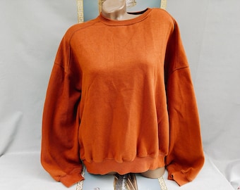 Könnte beinhalten: Verbrannt-oranges Sweatshirt mit Rundhalsausschnitt und langen Ärmeln. Das Sweatshirt hat eine lockere Passform sowie einen gerippten Saum und Bündchen. Der Stoff scheint ein weiches, leicht verwaschenes Material zu sein. Das Kleidungsstück wird auf einer Schaufensterpuppe präsentiert.