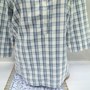 Pu&ograve; includere: Una camicia a quadri bianchi e blu con maniche a tre quarti. La camicia ha uno scollo abbottonato e una vestibilit&agrave; rilassata. Il motivo a quadri presenta una griglia di sottili linee blu su sfondo bianco. La camicia &egrave; realizzata in tessuto leggero.