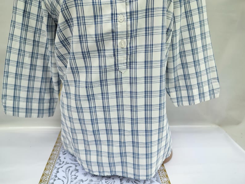 Pu&ograve; includere: Una camicia a quadri bianchi e blu con maniche a tre quarti. La camicia ha uno scollo abbottonato e una vestibilit&agrave; rilassata. Il motivo a quadri presenta una griglia di sottili linee blu su sfondo bianco. La camicia &egrave; realizzata in tessuto leggero.