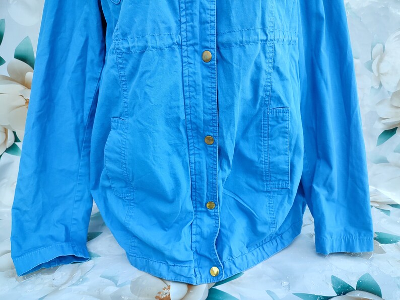 May include: A light blue jacket with a button closure and two pockets. The jacket has a drawstring at the waist.