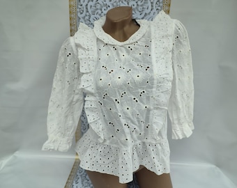 May include: White eyelet blouse with a ruffled neckline and long sleeves. The blouse has a floral pattern and a tiered ruffle at the bottom.