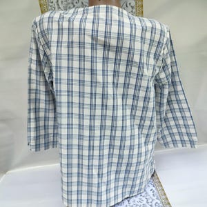 Pu&ograve; includere: Una camicia a maniche lunghe con un motivo a quadri blu e bianchi. La camicia ha un colletto classico e polsini con bottoni. Il tessuto sembra leggero e adatto alle temperature pi&ugrave; calde. La camicia &egrave; uno stile casual.