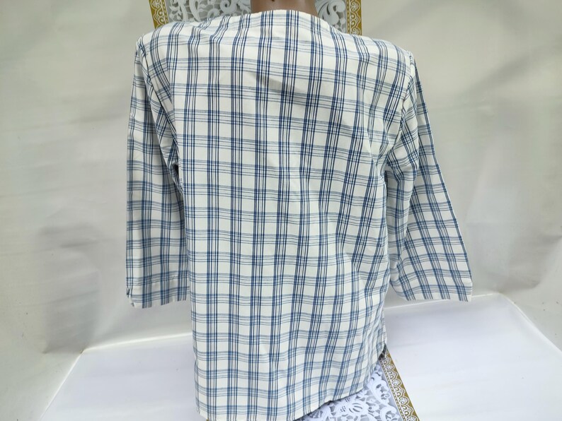 Pu&ograve; includere: Una camicia a maniche lunghe con un motivo a quadri blu e bianchi. La camicia ha un colletto classico e polsini con bottoni. Il tessuto sembra leggero e adatto alle temperature pi&ugrave; calde. La camicia &egrave; uno stile casual.
