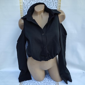 Peut inclure: Chemise noire à épaules dénudées avec des manches longues et un devant boutonné.