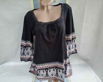 May include: Black top with three-quarter sleeves and a square neckline. The sleeves and hem feature a detailed pattern in shades of blue, pink, and brown. The neckline is trimmed with a braided design.