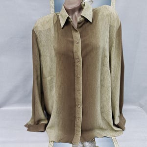 Puede incluir: Camisa abotonada marrón y beige claro, presentada en un maniquí. La camisa de manga larga tiene cuello y un patrón de rayas verticales. La tela parece ligera y ligeramente texturizada.