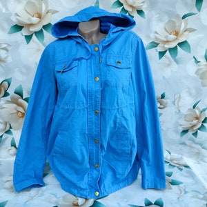May include: A light blue hooded jacket with a button closure and two front pockets. The jacket is made of a soft, lightweight fabric.