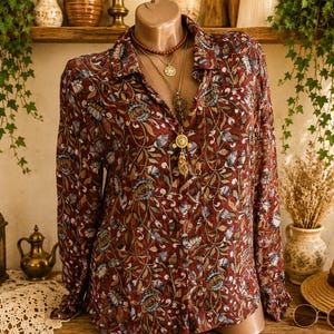 May include: A long-sleeved button-down shirt featuring a dark red base with a repeating pattern of stylised flowers, leaves, and vines in shades of blue, tan, and cream. The shirt has a classic collar and is displayed on a mannequin torso.