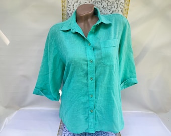 Puede incluir: Una camisa turquesa con botones, cuello y un bolsillo en el pecho. Las mangas están enrolladas y la camisa está hecha de una tela texturizada. La camisa se muestra en un maniquí.