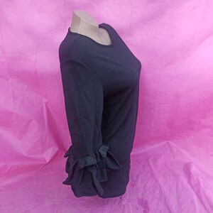 May include: Black long-sleeve shirt with ruffled cuffs. The shirt is on a pink background.