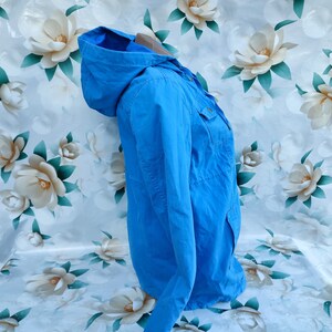 May include: A light blue hooded jacket with a zipper and button closure. The jacket has two pockets on the front and a single pocket on the left sleeve.