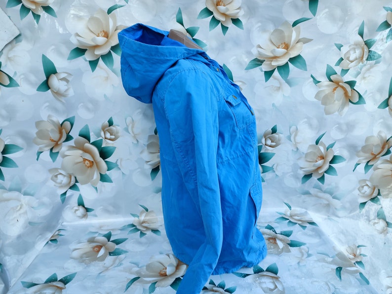 May include: A light blue hooded jacket with a zipper and button closure. The jacket has two pockets on the front and a single pocket on the left sleeve.