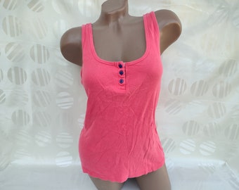 May include: A coral pink sleeveless tank top with a button closure down the front. The buttons are navy blue.