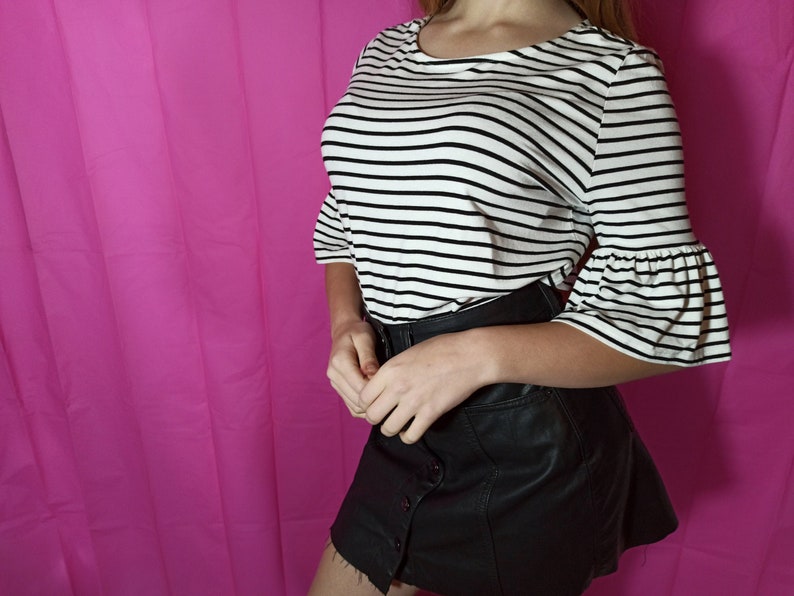 May include: A white and black striped shirt with bell sleeves and a black faux leather skirt.