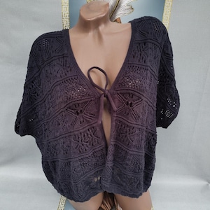 May include: Dark purple open-front knit cardigan with short sleeves. The cardigan features a V-neckline and a tie closure. The knit pattern includes openwork and decorative elements. The garment is displayed on a mannequin.