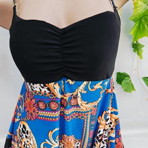 Puede incluir: Top negro con tirantes finos y corpi&ntilde;o fruncido, combinado con una falda azul con un estampado barroco dorado y rojo. La falda tiene un borde con estampado de leopardo.