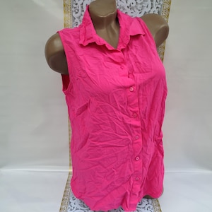 Puede incluir: Una camisa rosa sin mangas con botones y cuello.