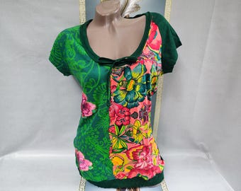 Puede incluir: Top de manga corta con diseño patchwork. El lado izquierdo es verde con un estampado floral, y el lado derecho es una vibrante mezcla de estampados florales rosas, amarillos y azules. El escote y las mangas están ribeteados en verde oscuro.