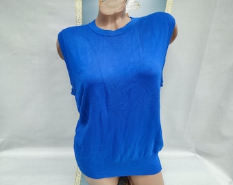 Puede incluir: Un suéter sin mangas de color azul real. La parte superior tiene cuello redondo y una textura lisa y tejida. La prenda se exhibe en un maniquí, mostrando su forma y ajuste. Esta parte superior es una prenda clásica.