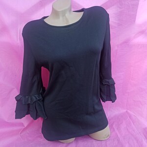 May include: A black long-sleeved shirt with ruffled sleeves. The shirt has a round neckline and is made of a soft, stretchy fabric.