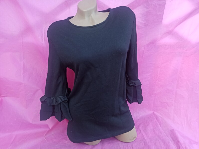 May include: A black long-sleeved shirt with ruffled sleeves. The shirt has a round neckline and is made of a soft, stretchy fabric.