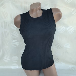 May include: A black ribbed vest top displayed on a mannequin. The sleeveless top has a round neckline and a fitted shape. The fabric has vertical ribbing, adding texture. The top is a solid black colour.