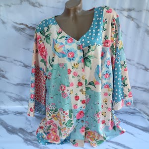 May include: A long-sleeved button-up shirt with a patchwork design featuring floral and polka dot patterns in shades of blue, pink, and white.