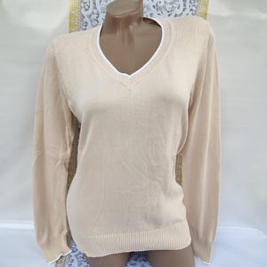 May include: A beige long-sleeved sweater with a white v-neck collar.
