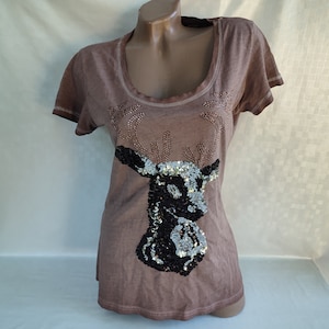 May include: A brown t-shirt featuring a sequined deer design. The deer is black and silver with a brown outline.