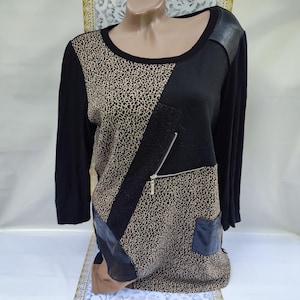 Può includere: Top nero a maniche lunghe con scollo tondo. Il top presenta un motivo leopardato, pannelli neri e una tasca con cerniera. Accenti in pelle sono visibili sulle spalle e sulla parte inferiore anteriore.