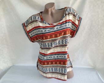 May include: A short-sleeved shirt with a colorful geometric pattern in shades of red, blue, white, and brown. The pattern is reminiscent of Native American designs.