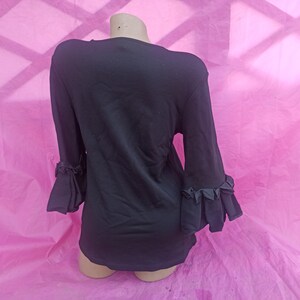 May include: Black long-sleeved shirt with ruffled detailing on the sleeves.