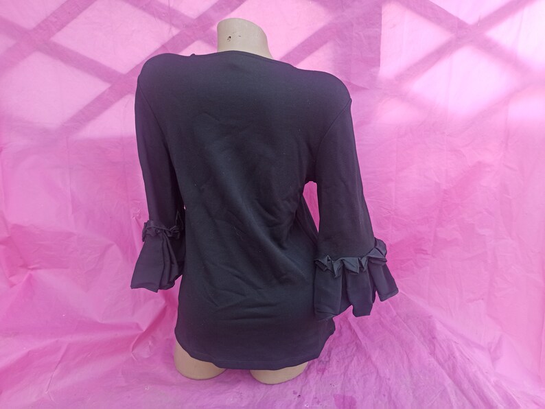 May include: Black long-sleeved shirt with ruffled detailing on the sleeves.