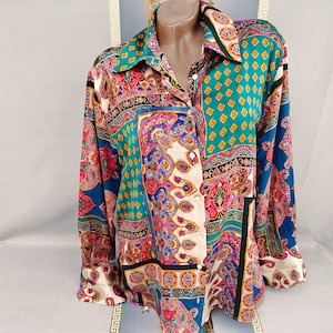 Puede incluir: Camisa abotonada con un vibrante estampado de cachemira en verde azulado, rosa, morado y azul. La camisa de manga larga presenta un cuello y una mezcla de diseños geométricos y florales, creando una declaración audaz y colorida.