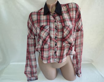 Puede incluir: Una camisa de manga larga a cuadros rojos y blancos con cuello negro. La camisa tiene una longitud recortada y dos bolsillos en el pecho.